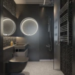 Kinkiet Ringa D90 w kolorze białym, z jedną diodą LED o mocy 45W, umieszczony na tle ciemnej łazienki. Okrągły kształt i subtelne podświetlenie tworzą nowoczesny efekt, montowany na ścianie obok lustra. Wysoka klasa ochrony IP44.