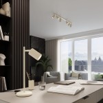 Beżowa lampka stołowa Karbon z kloszem o żebrowanej fakturze, umieszczona na stabilnym okrągłym podstawie. Ujęcie z boku, na biurku, w nowoczesnym wnętrzu z roślinnością i dużymi oknami. W tle widoczna szara kanapa i półka z książkami.