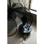 Lampa wisząca Styrka 1xE27 w kolorze czarnym z dymnym kloszem, z charakterystycznymi, szerokimi, półprzezroczystymi elementami. Ujęcie z góry, ukazujące detale klosza oraz okrągłą podstawę. W tle widać drewnianą podłogę i szklane akcesoria.