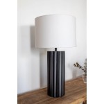 Lampa stołowa Hashira z czarną, teksturowaną podstawą w pionowe żłobienia oraz białym, okrągłym kloszem. Ujęcie z boku, stojąca na drewnianym stole, w tle jasna ściana. Wymiary i detale podstawy nie są widoczne.