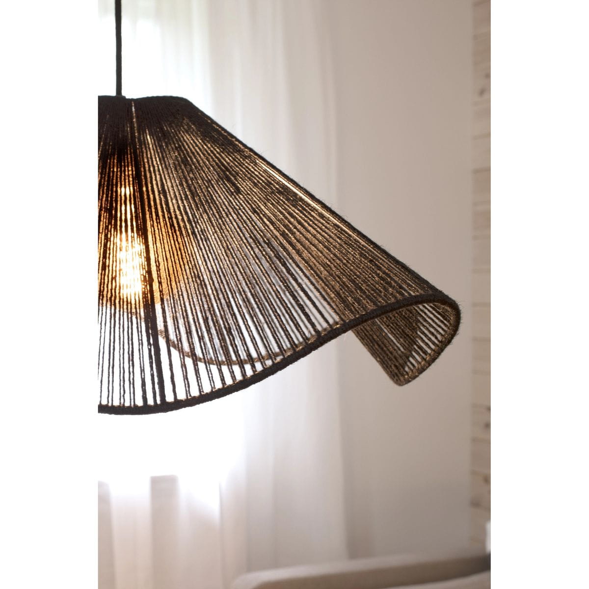 Lampa wisząca Nami z czarnym kloszem, wykonanym z cienkich włókien, tworzy efektowne oświetlenie. Ujęcie zbliżone na klosz, delikatnie podświetlony od wewnątrz. Tło jasne, z zasłonami, co podkreśla elegancję lampy.