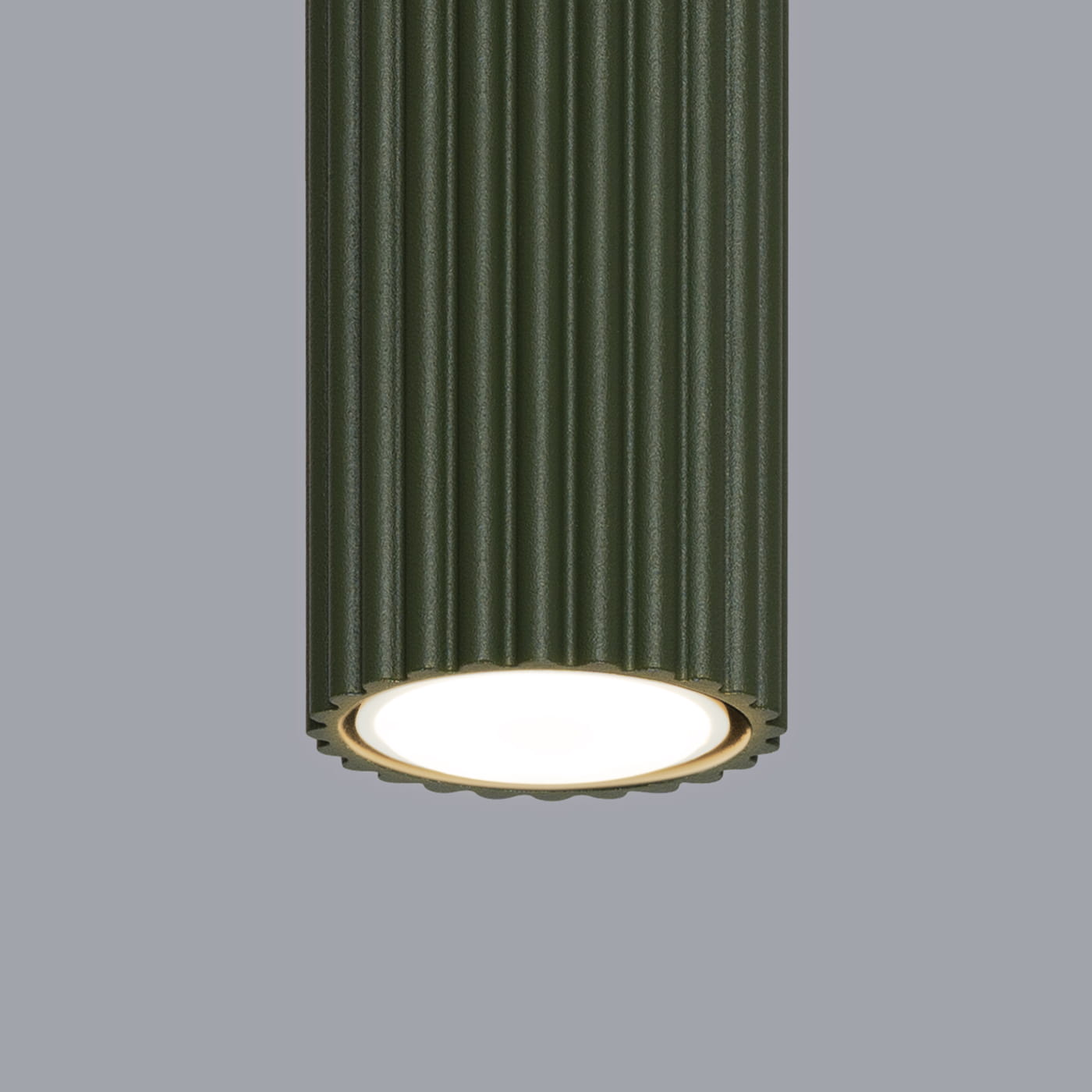 Lampa sufitowa Karbon 60, kolor oliwkowy, z cylindrycznym kloszem w delikatne żłobienia. Zamontowana żarówka GU10 w centralnej części, emitująca światło. Kąt ujęcia z dołu, na jednolitym, szarym tle.
