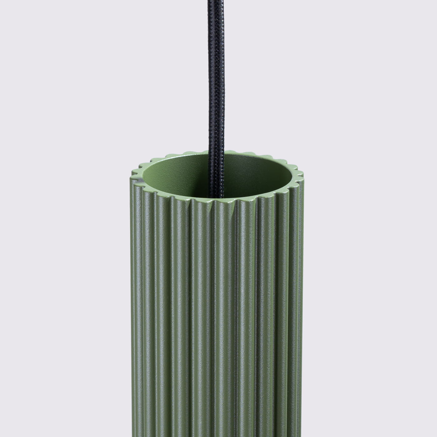 Lampa wisząca Karbon 2 w kolorze oliwkowym, z cylindrycznym kloszem o żłobionej fakturze. Ujęcie z bliska, skupione na górnej części lampy z przewodem w czarnym oplocie. Wnętrze klosza ma gładką powierzchnię.