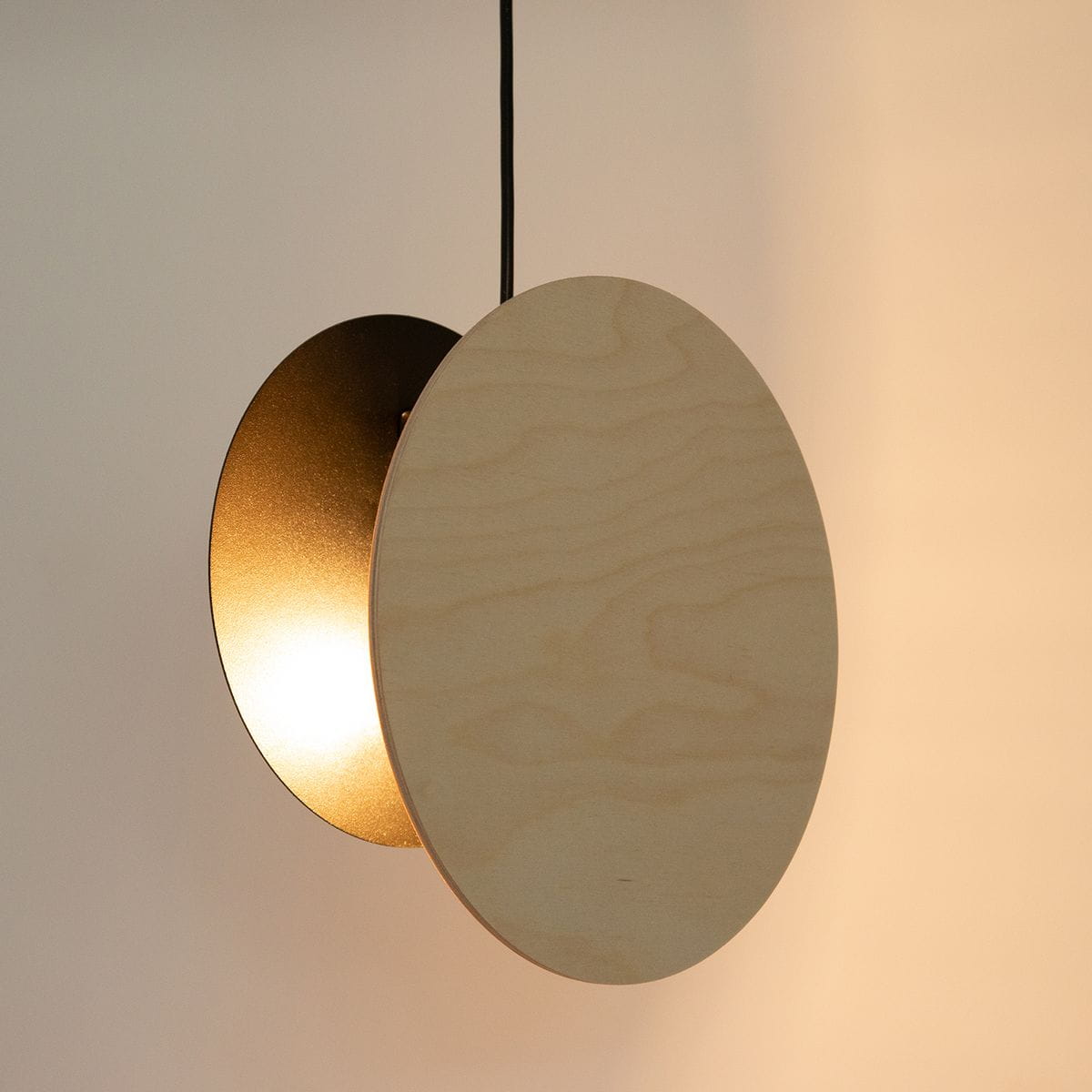 Lampa wisząca Tola z okrągłą, brzozową osłoną i czarnym metalowym elementem. Zawieszona na czarnym przewodzie, emitująca ciepłe światło. Prosta, nowoczesna forma, idealna do różnych aranżacji wnętrz.