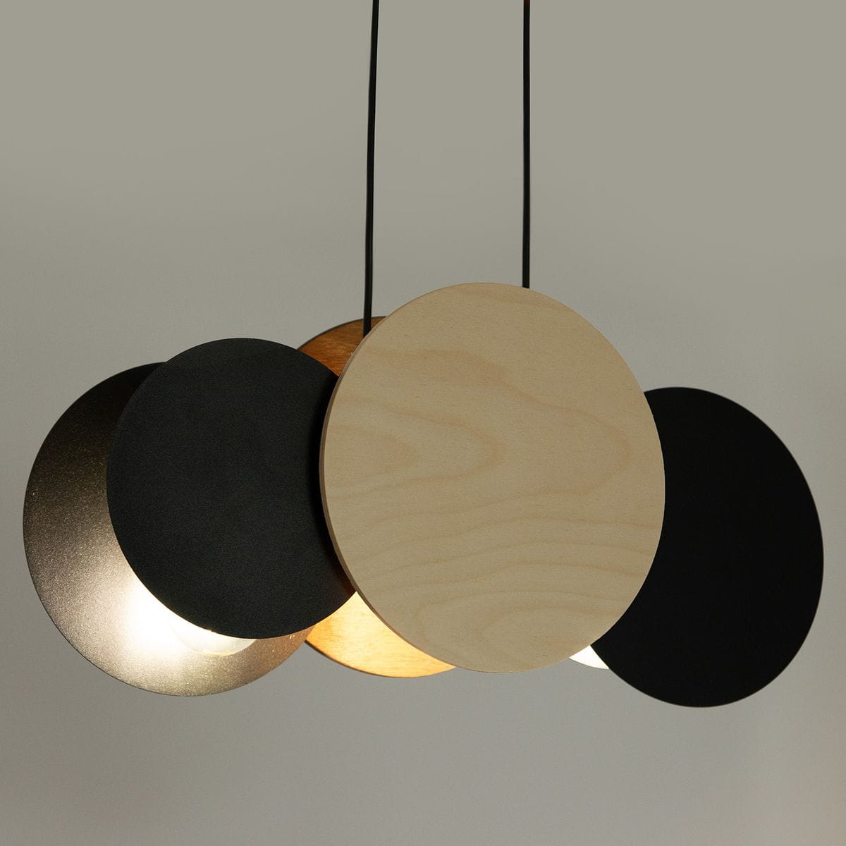 Lampa wisząca Tola z trzema okrągłymi kloszami: dwa czarne (matowy i metaliczny) oraz jeden brzozowy. Klosze zawieszone na czarnych przewodach, tworzą nowoczesny, minimalistyczny design. Oświetlenie z trzonkiem E27, idealne do nowoczesnych wnętrz.
