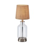Lampa stołowa Costero z przezroczystym kloszem i naturalnym abażurem. Podstawa w kolorze srebrnym, kształt butelkowy. Wysokość około 50 cm, idealna do wnętrz w stylu skandynawskim lub nowoczesnym.