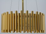 Lampa wisząca Narni 4xE27 w kolorze złotym, zbudowana z prostokątnych, cylindrycznych elementów, wisząca na cienkich linkach. Kąt ujęcia z góry, ukazujący szczegóły struktury i wykończenia. Tło jednolite.