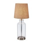 Lampa stołowa Costero z przezroczystym kloszem i naturalnym abażurem. Kształt butelki, metalowa podstawa w kolorze srebrnym. Ujęcie frontalne, stojąca, idealna na stół lub biurko. Wysokość około 50 cm.