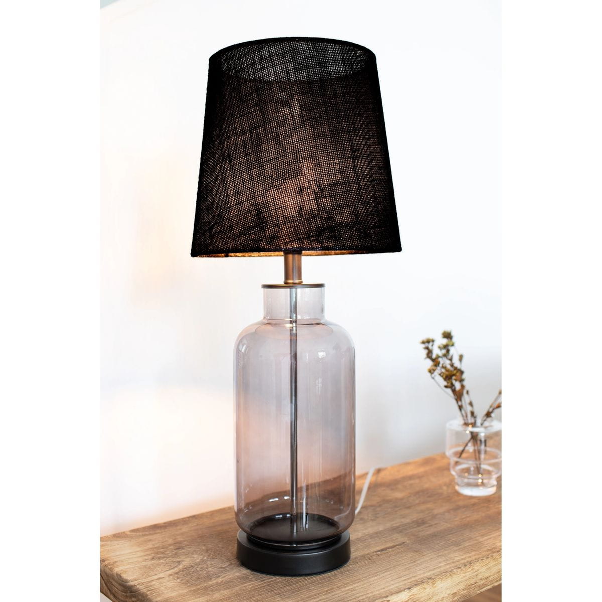 Lampa stołowa Costero z dymnym, szklanym kloszem i czarnym abażurem, stojąca na okrągłej, matowej podstawie. Wysoka, elegancka konstrukcja z metalowym elementem, idealna do nowoczesnych wnętrz.