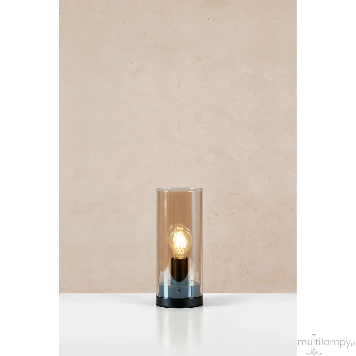 Post lampa stołowa w kolorze czarnym z bursztynowym kloszem, o cylindrycznym kształcie. Widoczna żarówka E27 wewnątrz, umieszczona na okrągłej podstawie. Ujęcie frontalne na tle jasnej ściany.