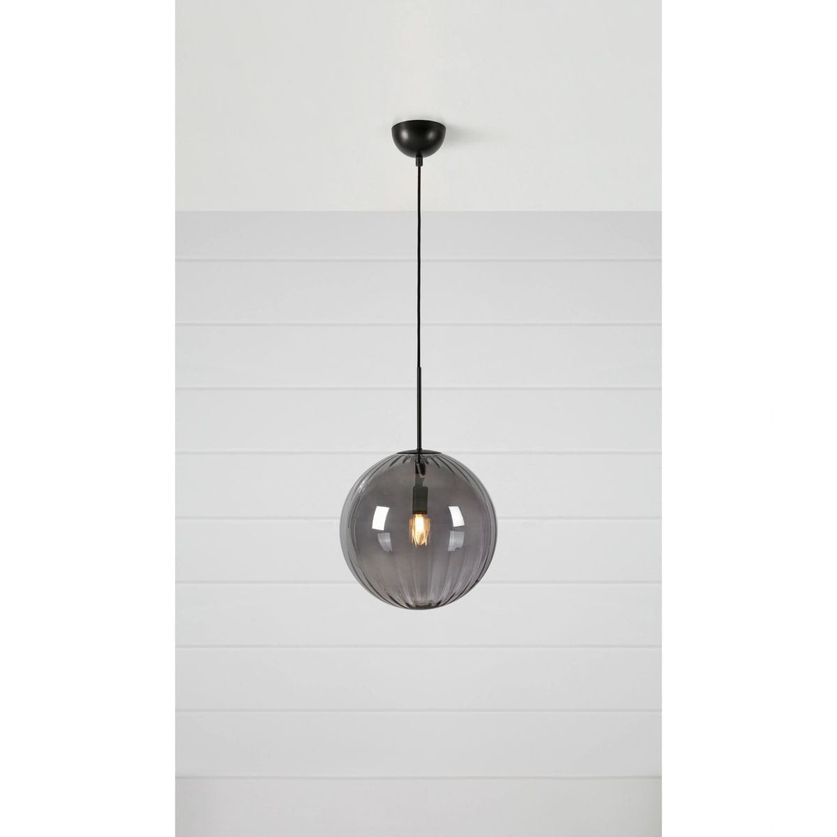 Lampa wisząca Fengari 1xE14 w kolorze czarnym z dymionym kloszem. Okrągły kształt z szarym, przezroczystym szkłem, zawieszona na cienkim czarnym przewodzie. Widoczna żarówka wewnątrz klosza. Ujęcie frontalne na białym tle.