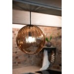 Lampa wisząca Fengari z jednym gniazdem E14, w kolorze antycznego mosiądzu z bursztynowym kloszem. Okrągły, szklany klosz z teksturą, zawieszony na czarnym przewodzie. Widoczne tło z cegły i elementy aranżacji wnętrza.