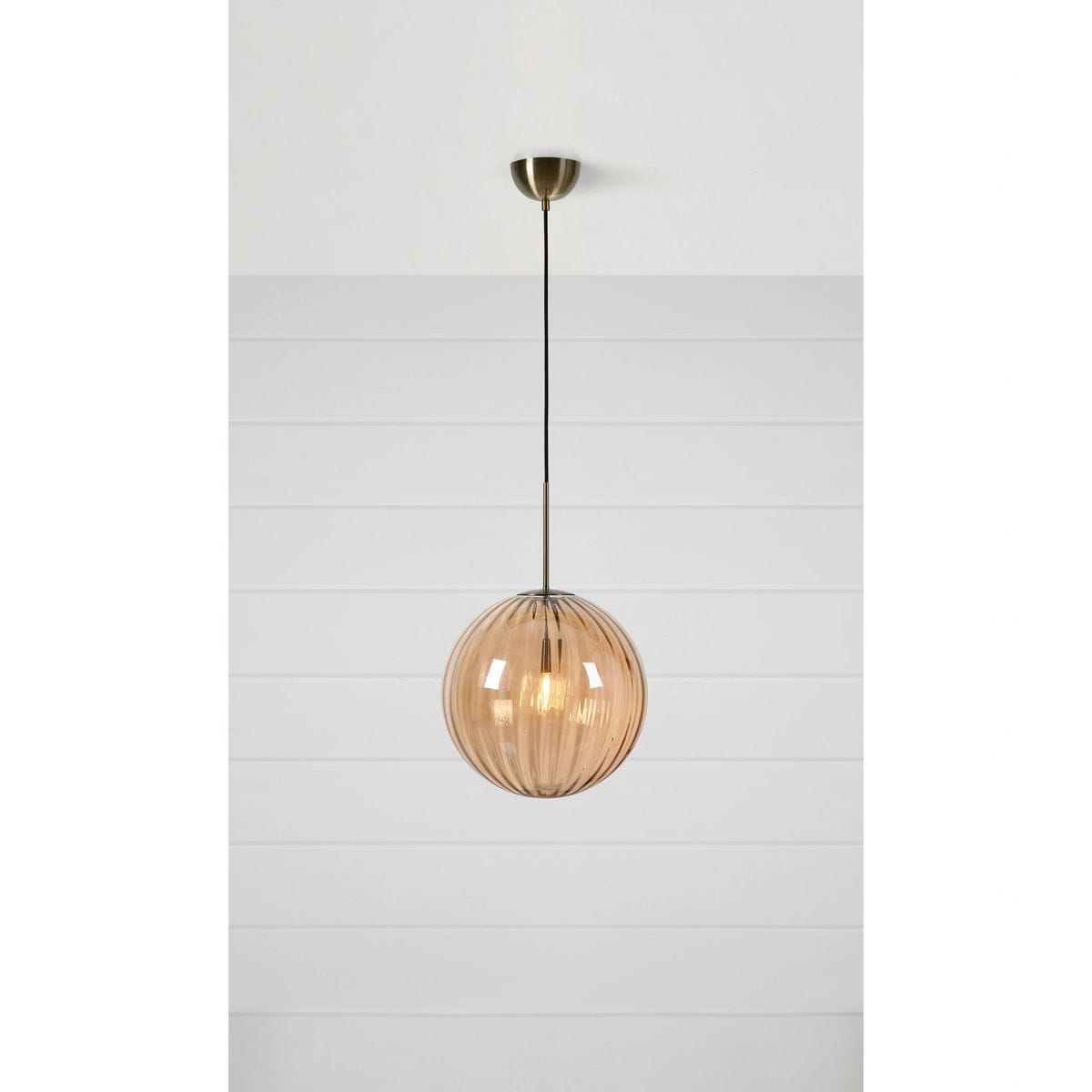 Lampa wisząca Fengari 1xE14 w kolorze antycznego mosiądzu z bursztynową, szklaną kulą. Kula ma delikatne, żłobione wykończenie i jest zawieszona na cienkim kablu. Produkt umieszczony na jasnym tle, ukazując jego kształt i strukturę.