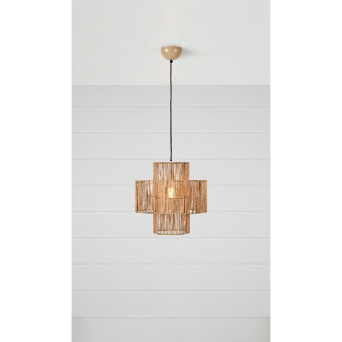 Lampa wisząca Soga 1xE27 w naturalnym kolorze, z plecionego materiału, w kształcie krzyża. Zawieszona na czarnym przewodzie, z zaokrąglonym mocowaniem sufitowym. Widoczne ciepłe światło w środku. Tło białe, proste.