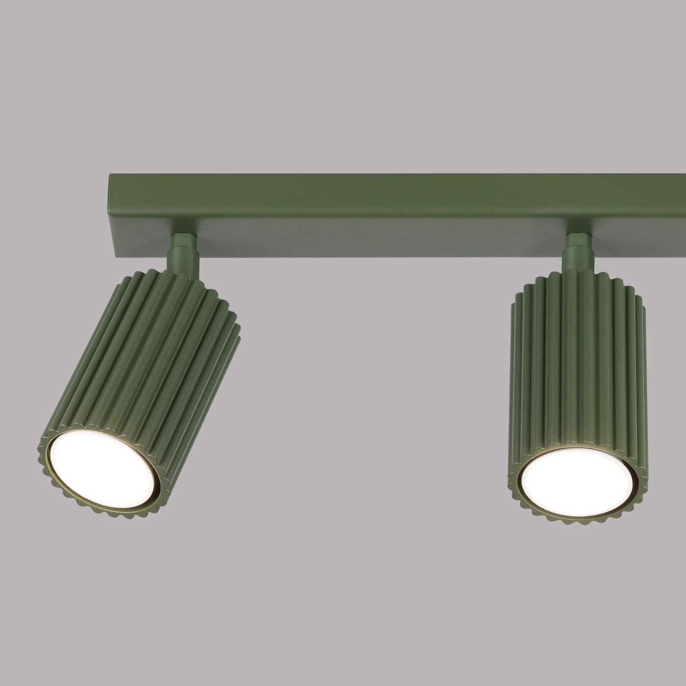 Lampa sufitowa Karbon w kolorze oliwkowym z trzema reflektorami GU10. Ujęcie z boku, pokazujące detale żłobień na obudowach reflektorów. Mocowana na prostokątnej podstawie, na jednolitym tle.