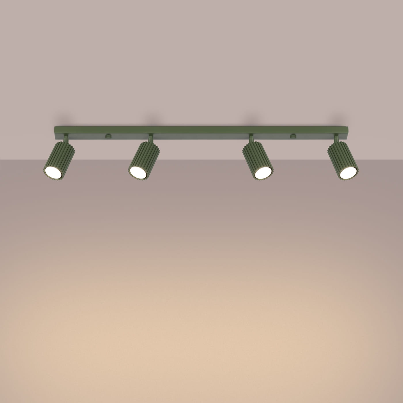 Lampa sufitowa Karbon L w kolorze oliwkowym, z czterema reflektorami GU10. Ujęcie frontalne, zamontowana na ścianie, z widocznymi żeberkami na oprawach. Reflektory skierowane w dół, emitują jasne światło. Tło w odcieniach beżu.