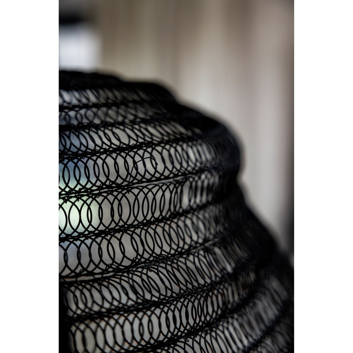 Lampa wisząca Tazza w kolorze czarnym, wykonana z metalowej siatki w formie okrągłego klosza. Ujęcie z boku, zbliżenie na strukturę materiału. Widoczne przestrzenne wzory, które tworzą efektowną iluminację.