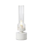 Lampa stołowa Kandella w kolorze białym i przezroczystym, z cylindrycznym kloszem. Posiada podstawę z białego materiału oraz dekoracyjną obręcz z wzorem przypominającym płomień. Źródło światła E14 umieszczone wewnątrz. Stoi na płaskiej powierzchni.