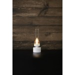 Lampa stołowa Kandella z oprawą w białym kolorze i przezroczystym kloszem, z żarówką E14. Ujęcie frontalne, na ciemnym blacie. Klosz w kształcie tuby, z delikatnym wzorem u podstawy, emituje ciepłe światło.