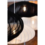 Czarna lampa wisząca Florence D75 z oprawą na jedną żarówkę E27. Posiada zaokrąglony klosz z cienkimi, poziomymi paskami, ukazującym źródło światła. W tle widoczna biała lampa o podobnym kształcie. Ujęcie z boku, wisząca w nowoczesnym wnętrzu.