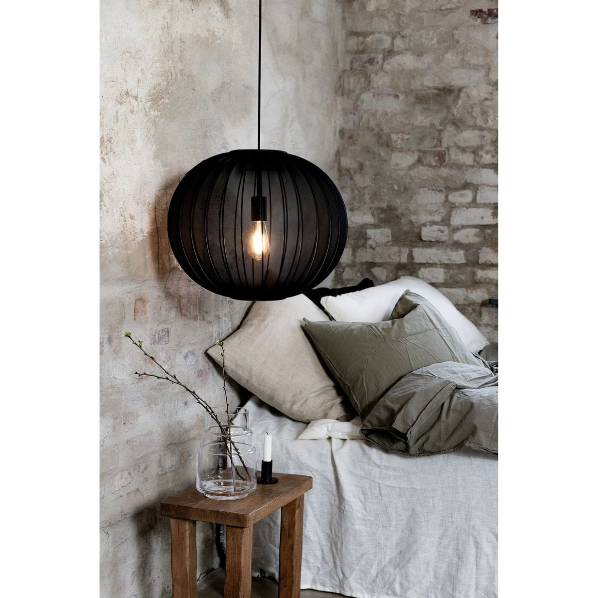 Lampa wisząca Florence D50 w kolorze czarnym z okrągłym kloszem, zawieszona nad łóżkiem. W tle widoczne poduszki w różnych odcieniach, stół z drewnianą nogą oraz szklany wazon z gałązką. Oświetlenie z żarówką E27.