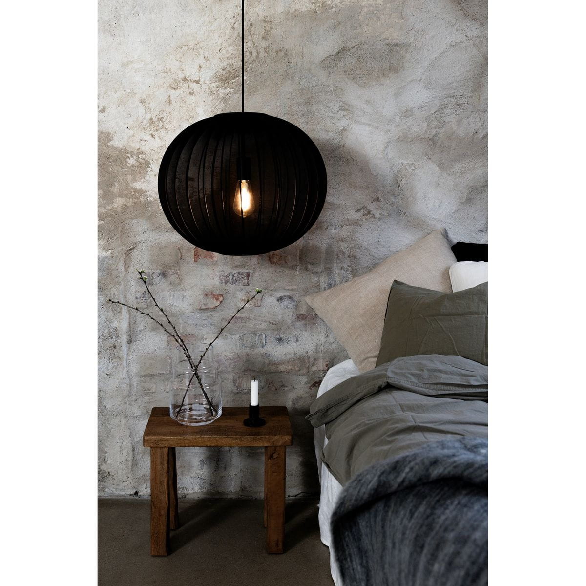 Lampa wisząca Florence D50 w kolorze czarnym z kloszem w kształcie okrągłym, zawieszona nad drewnianym stolikiem. Wnętrze w stylu industrialnym z widoczną fakturą ściany. Widoczna żarówka E27 wewnątrz lampy.