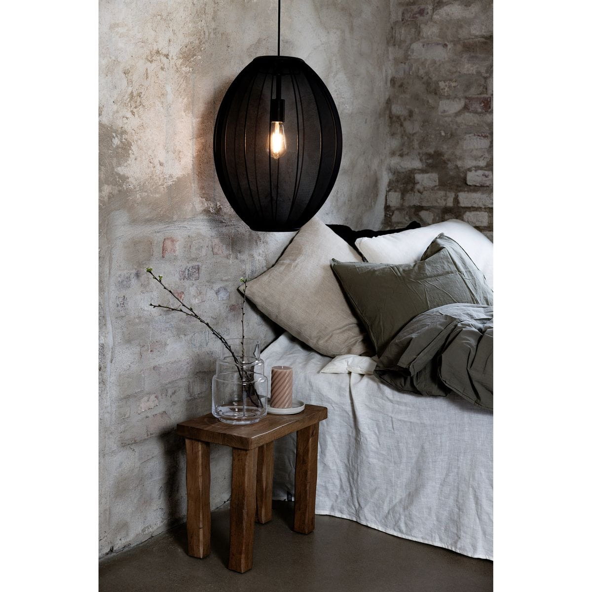 Czarna lampa wisząca Florence D40 z oprawą na żarówkę E27, o zaokrąglonym kształcie i teksturowanej powierzchni. Zawieszona nad drewnianym stolikiem obok łóżka, w aranżacji z naturalnymi tkaninami i dodatkami.