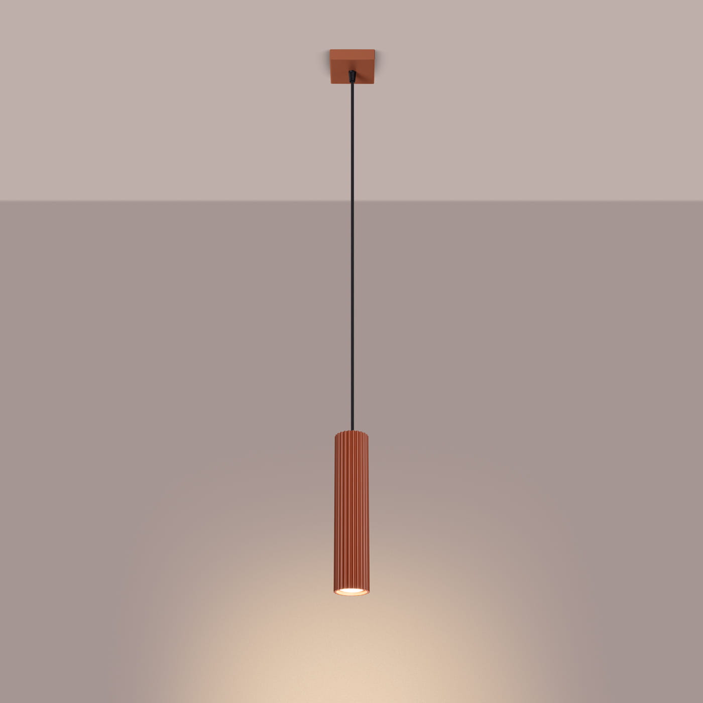 Lampa wisząca Karbon 1, kolor ochra czerwona, z cylindrycznym, żebrowanym kloszem, zawieszona na czarnym przewodzie. Widoczna żarówka GU10 emitująca ciepłe światło, montowana do sufitu. Tło w stonowanej kolorystyce.