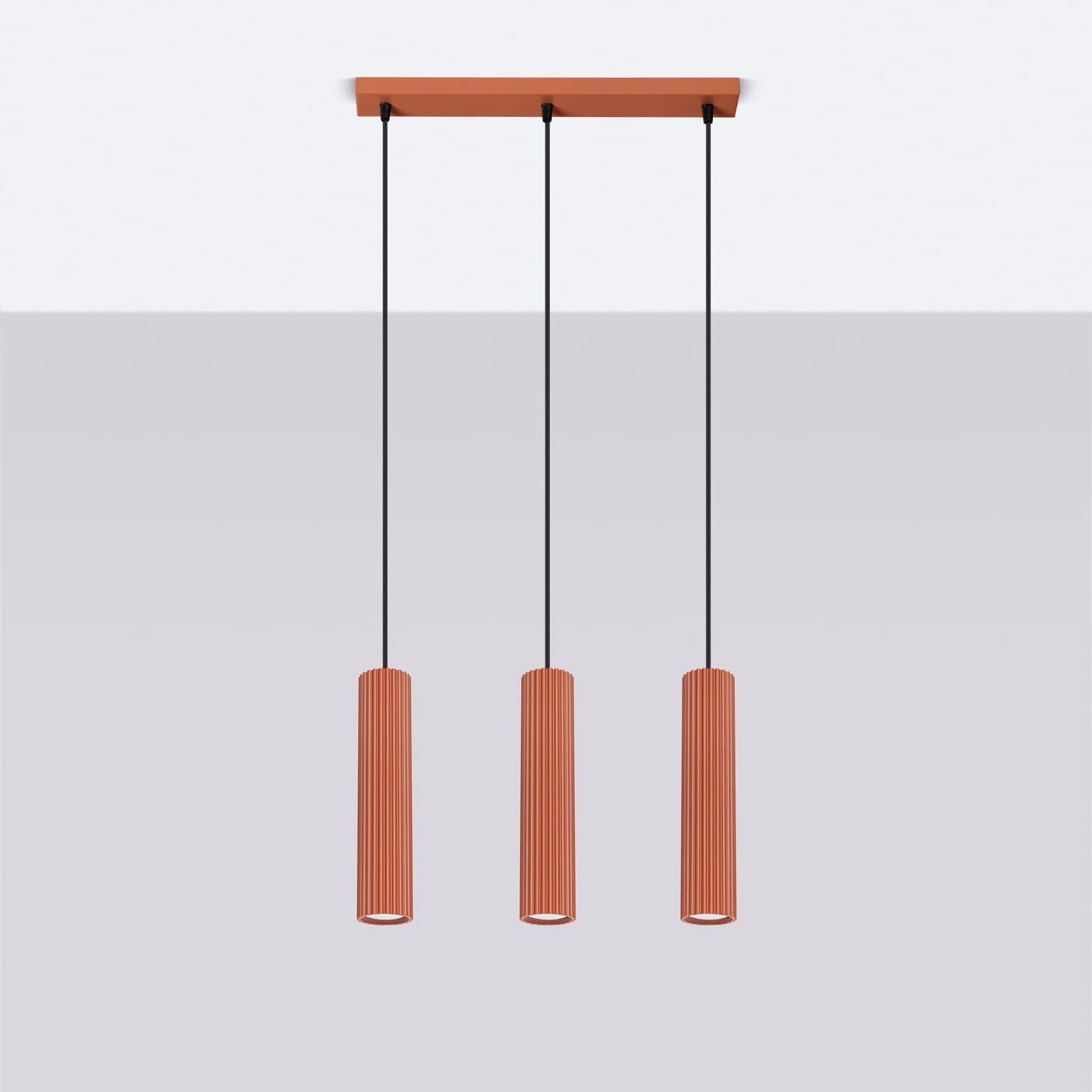 Lampa wisząca Karbon 3 z trzema lampami GU10 w kolorze ochry czerwona, z cylindrycznymi kloszami o żebrowanej fakturze, zawieszona na czarnych przewodach. Montaż sufitowy, w minimalistycznym stylu, na jasnym tle.