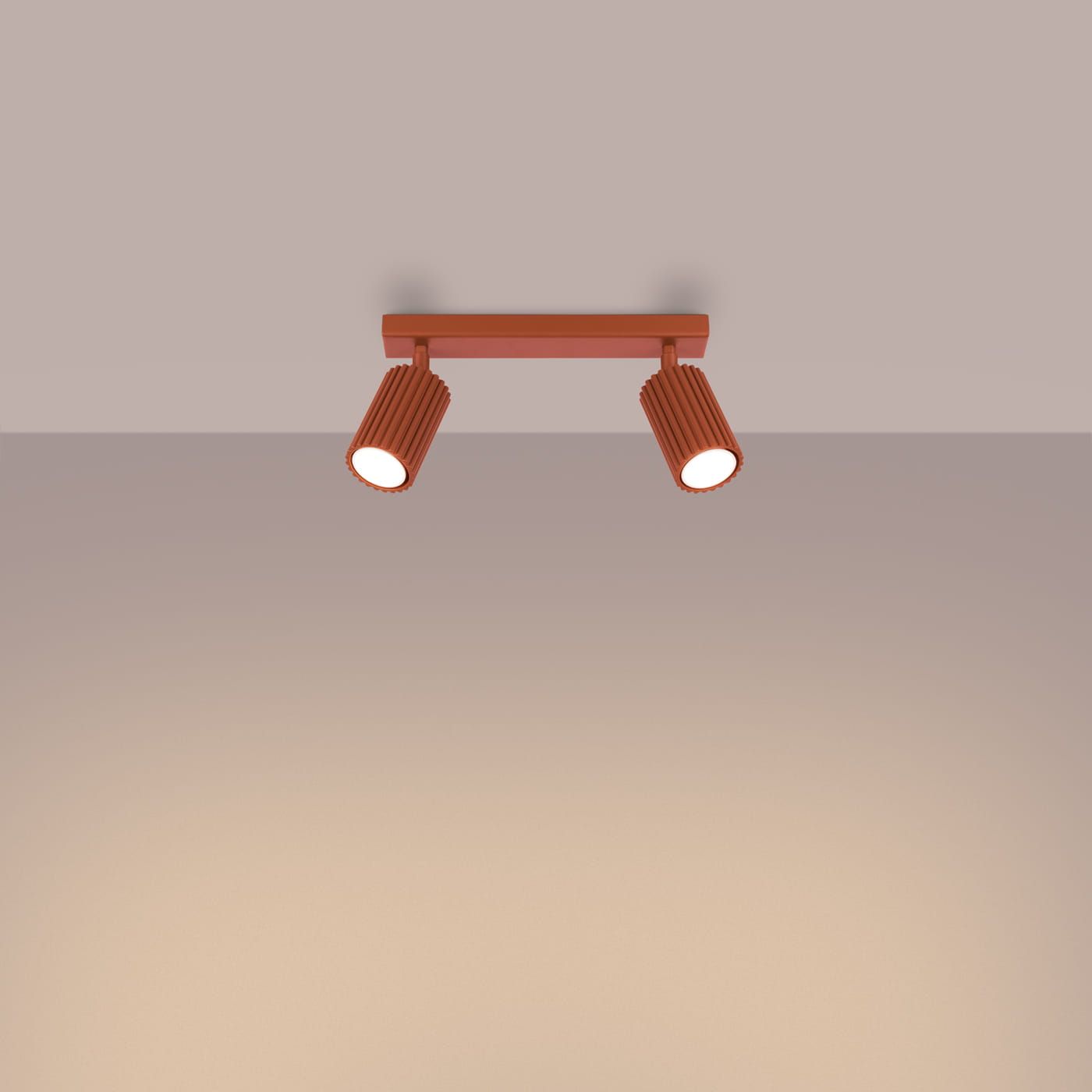 Lampa sufitowa Karbon w kolorze ochra czerwona z dwoma ruchomymi reflektorami GU10. Ułożona równolegle do sufitu, z widoczną teksturą na obudowach lamp. Tło w jasnym odcieniu, co podkreśla kolor lampy.