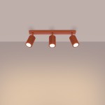 Lampa sufitowa Karbon w kolorze ochra, z trzema reflektorami GU10. Reflektory mają teksturowaną, cylindryczną formę, zamontowane na prostokątnej podstawie. Ujęcie frontalne, produkt wisi na suficie, na jednolitym tle.
