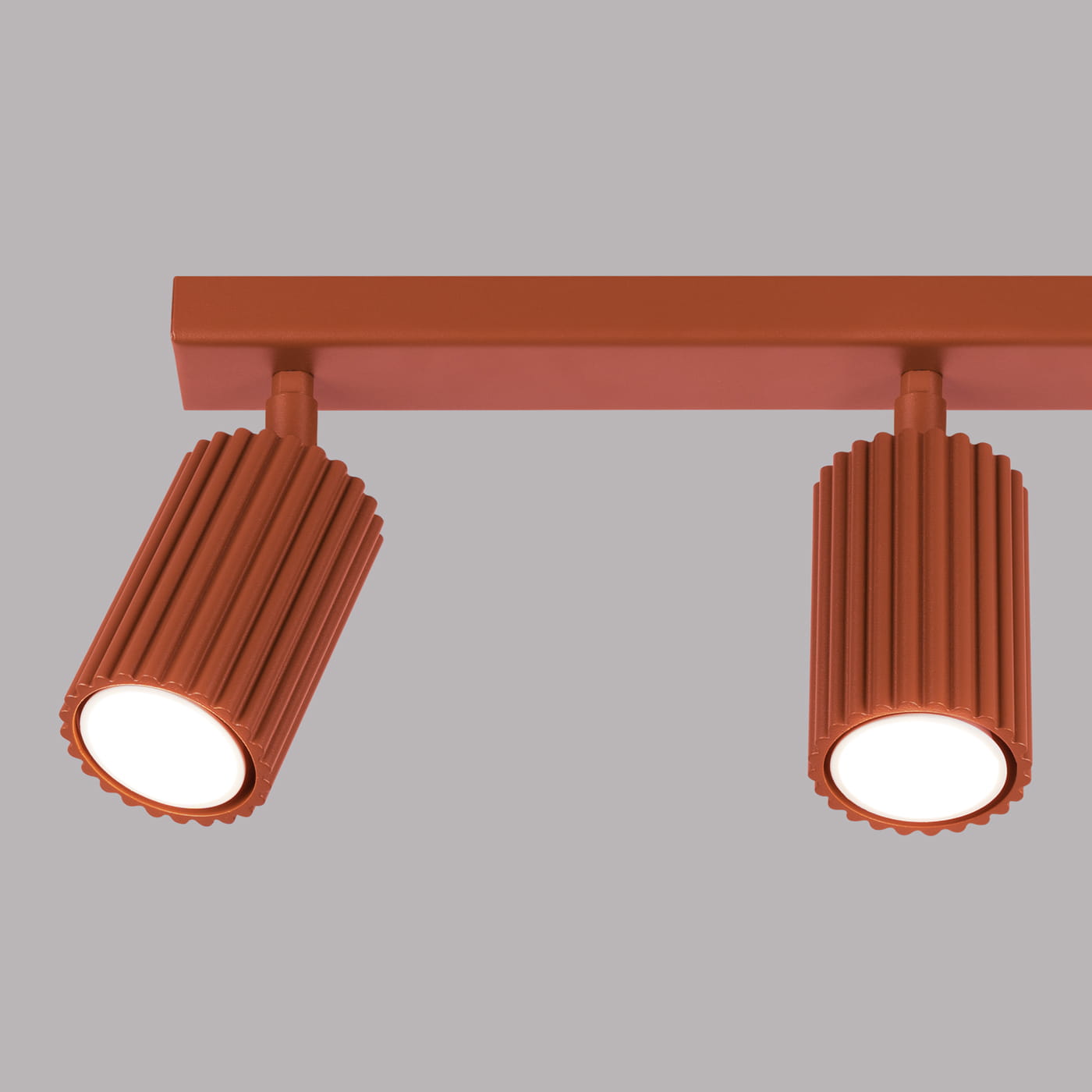 Karbon lampa sufitowa (spot) 3xGU10 w kolorze ochra czerwona, z trzema cylindrycznymi reflektorami o żłobionej teksturze, zamontowana na prostokątnej podstawie. Reflektory skierowane w dół, na jednolitym szarym tle.