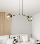 Lampa wisząca Skiva z dwoma okrągłymi kloszami, czarna metalowa konstrukcja z jasnym drewnem. Ujęcie frontalne, zawieszona na cienkich linkach. Tło w jasnych odcieniach, w aranżacji salonu z jasną sofą i poduszkami.