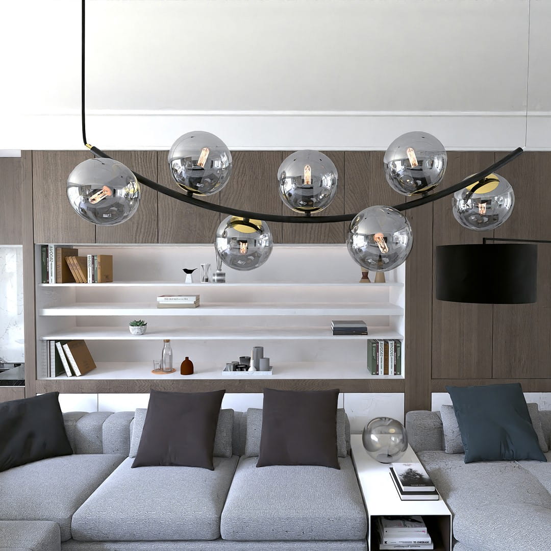 Lampa wisząca Ritz z siedmioma kulistymi kloszami w kolorze czarnym i grafitowym, zawieszona na łukowatej konstrukcji. Klosze mają metaliczny połysk, a lampa znajduje się nad szarym narożnikiem w nowoczesnym wnętrzu.