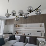 Lampa wisząca Ritz z siedmioma oprawami na żarówki E14 w kolorze czarnym i grafitowym. Ułożona na zakrzywionej, metalowej podstawie. Szklane klosze w kształcie kul odbijają światło, nadając nowoczesny charakter wnętrzu.