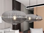 Lampa wisząca Coco 1xE27 w kolorze czarnym i grafitowym, z przezroczystym, falistym kloszem. Zawieszona na cienkim metalowym przewodzie, w nowoczesnym wnętrzu z jasnymi ścianami i sofą. Widoczne źródło światła w środku klosza.