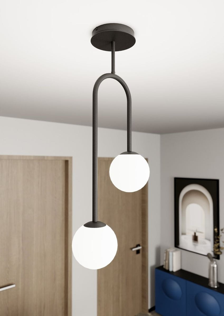 Lampa sufitowa Atria z dwoma opalowymi kulami, zamocowana na czarnym metalowym stelażu. Wisi pod sufitem w nowoczesnym wnętrzu, z białym tłem i drewnianymi drzwiami w tle. Widać również niebieską komodę z dekoracjami.