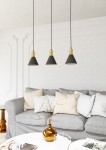 Lampa wisząca Rosa z trzema kloszami w kształcie stożka, czarna z złotymi akcentami u góry. Zawieszona na cienkich kablach, w nowoczesnym wnętrzu z szarym sofą i dekoracjami na stole.