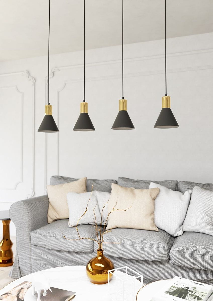 Lampa wisząca Rosa 4xE27 w kolorze czarnym i złotym, z czterema stożkowymi kloszami zawieszonymi na cienkich czarnych przewodach. Produkt umieszczony nad szarym sofą z poduszkami w różnych odcieniach, na tle jasnej ściany.