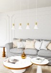 Lampa wisząca Rosa z czterema kloszami w białym kolorze i złotymi detalami, zawieszona na długich linkach. Widoczna w nowoczesnym wnętrzu, nad szarym narożnikiem i okrągłym stolikiem kawowym. Tło jasne, minimalistyczne.