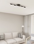 Czarna lampa sufitowa 4xGX53 zamontowana na suficie, składająca się z prostokątnej podstawy oraz czterech okrągłych źródeł światła. Ujęcie z boku, w tle widoczny jasny salon z sofą i lampą podłogową.