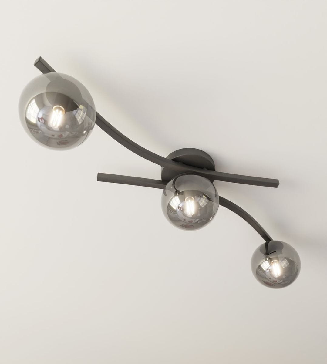 Lampa sufitowa Opus z trzema oprawkami E14, w kolorze czarnym i grafitowym. Posiada trzy szklane klosze w kształcie kul, zamontowana na podłużnej, lekko zakrzywionej podstawie. Kąt ujęcia z góry, na jednolitym tle.
