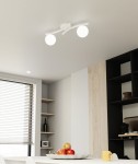 Lampa sufitowa Opus z dwoma opalowymi kloszami E14, zamontowana na białej podstawie. Ujęcie z dołu, ukazujące nowoczesny design i sposób oświetlenia wnętrza. W tle widać jasny stół z owocami oraz regały.