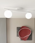Lampa sufitowa Opus z dwoma opalowymi kulami na białej, zakrzywionej podstawie. Ujęcie z dołu, ukazujące równomierne rozmieszczenie źródeł światła oraz minimalistyczny design. Tło w neutralnych kolorach z dekoracją w odcieniu czerwonym.