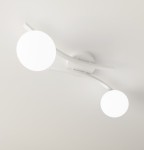 Biała lampa sufitowa Opus z dwoma okrągłymi, opalowymi kloszami. Ułożona na suficie, z delikatnymi, zakrzywionymi ramionami. Klosze emitują miękkie światło, tworząc nowoczesny akcent w aranżacji wnętrza.