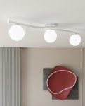 Lampa sufitowa Opus z trzema opalowymi kulami E14 w białej oprawie. Ujęcie z góry, z zamontowanym sufitem. Kuliste klosze równomiernie rozmieszczone na delikatnym, zakrzywionym stelażu. Tło w neutralnych kolorach, z dekoracją na ścianie.