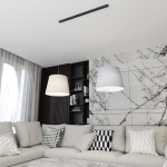 Lampa wisząca Epoca z dwoma kloszami w kolorze szarym i jasnym, zawieszona na czarnej listwie. Klosze mają cylindryczny kształt, a w tle widoczne są elementy nowoczesnego wnętrza z szaro-białą ścianą i sofą z poduszkami.