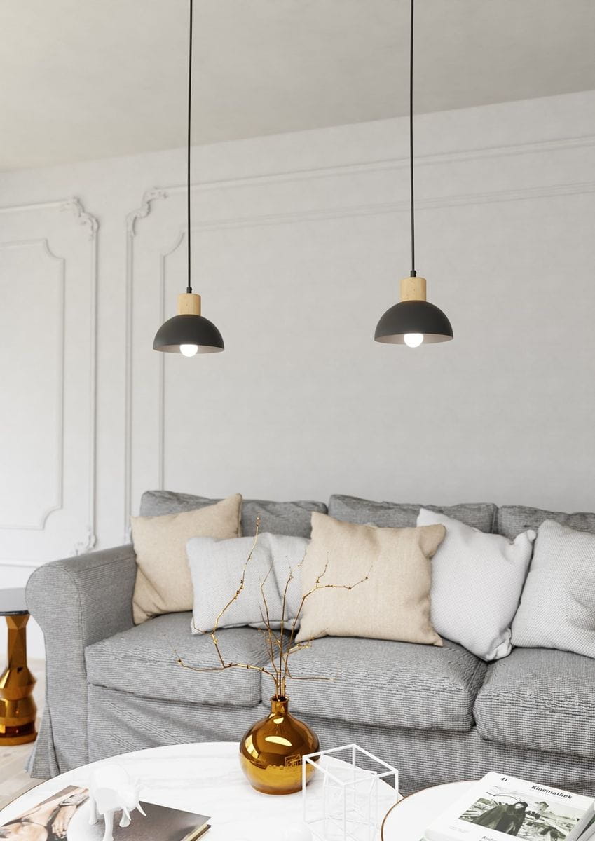 Lampa wisząca Seco 1xE27 w kolorze czarnym z jasnym drewnem, zawieszona na czarnym przewodzie. Okrągła, metalowa czasza z drewnianym elementem u góry. W tle szary narożnik z poduszkami i stół kawowy z dekoracjami.