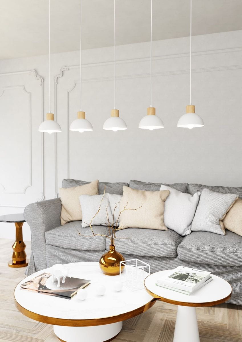 Lampa wisząca Seco z pięcioma białymi kloszami w jasnym drewnie, zawieszona na białych kablach. Klosze mają prosty, okrągły kształt. W tle widoczna szara sofa z poduszkami oraz stolik kawowy z okrągłym blatem.