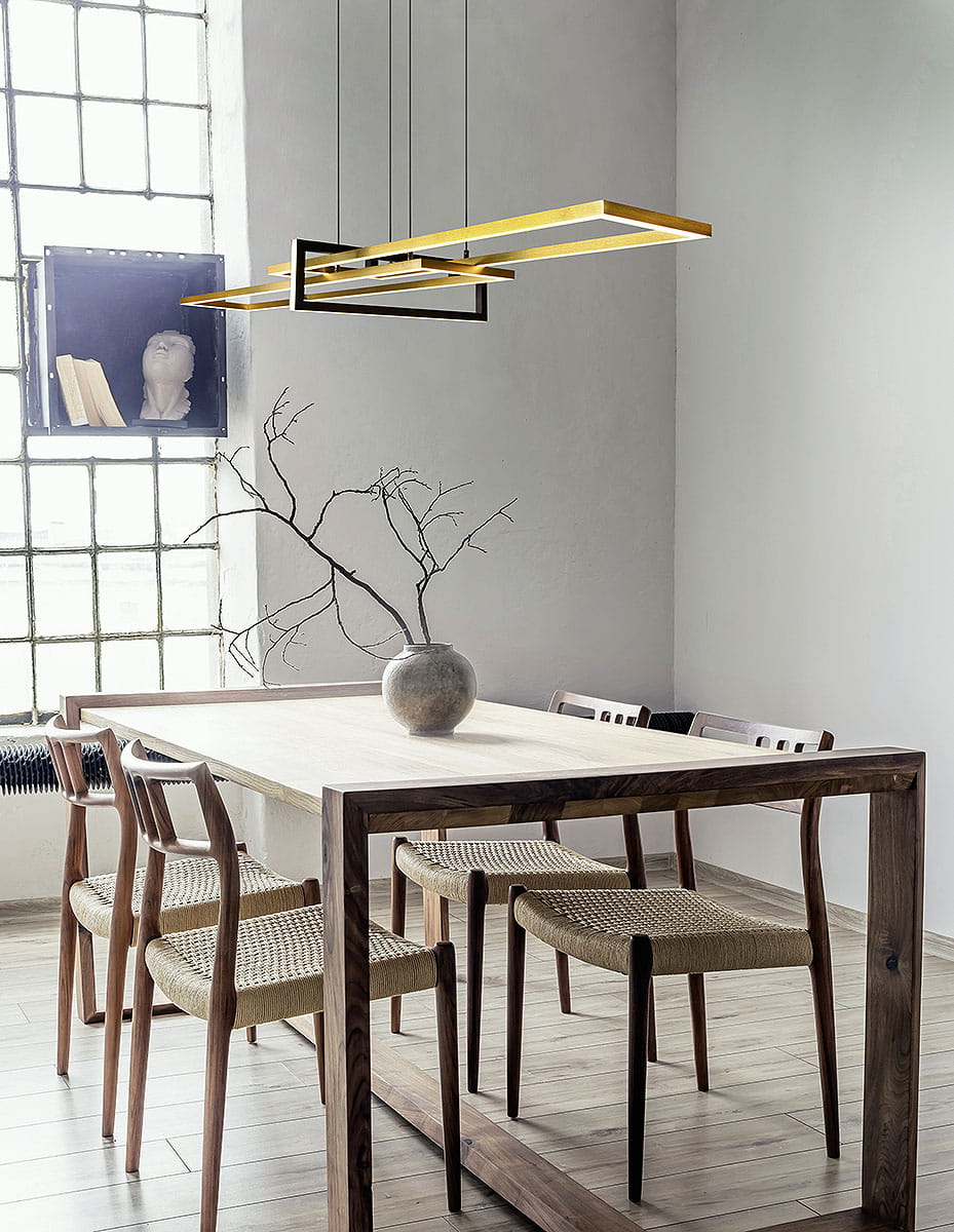 Salinas LED lampa wisząca 3-punktowa w mosiężnym i czarnym wykończeniu. Zawieszona nad drewnianym stołem, z trzema prostokątnymi ramkami, w nowoczesnym wnętrzu z naturalnym światłem, obok wazonu i minimalistycznych krzeseł.